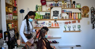 A hairdresser braids a customer's hair at a beauty salon, in downtown Caracas, Venezuela, Sept. 1, 2021. (AFP Photo)