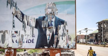 Two young boys walk past a torn billboard of the former president of Guinea, Alpha Conde, in Conakry, Guinea, Sept. 16, 2021. (AFP Photo)