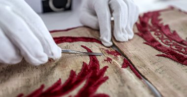 A close-up of a hand of a restorer while working on Sultan Suleiman I's caftan at the National Palaces Textile Workshop, Istanbul, Turkey, Sept. 16, 2021. (AA Photo)