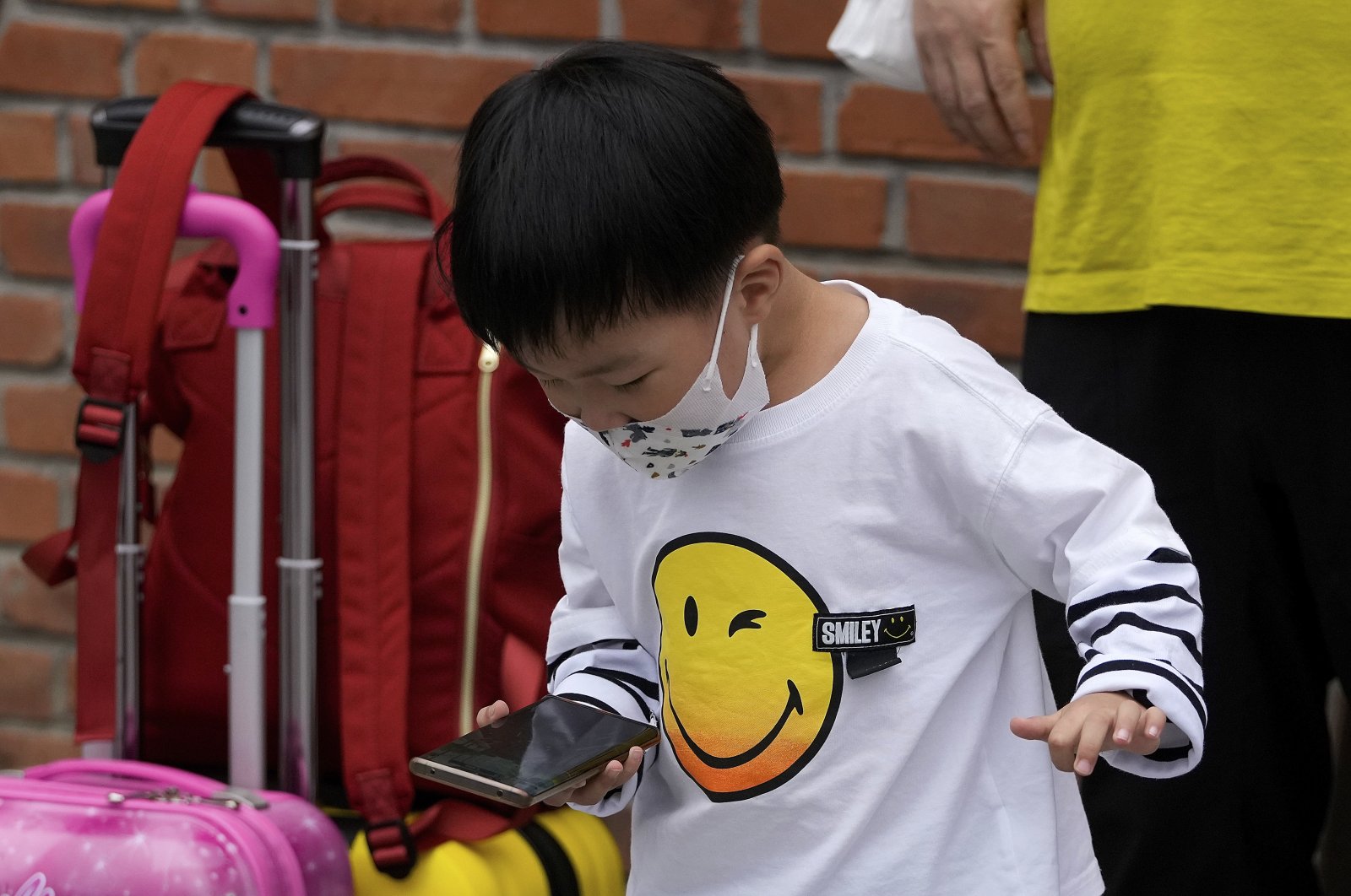 A child wearing a face mask plays a game on a smartphone next to his relative in Beijing, China, Sept. 12, 2021. (AP Photo)