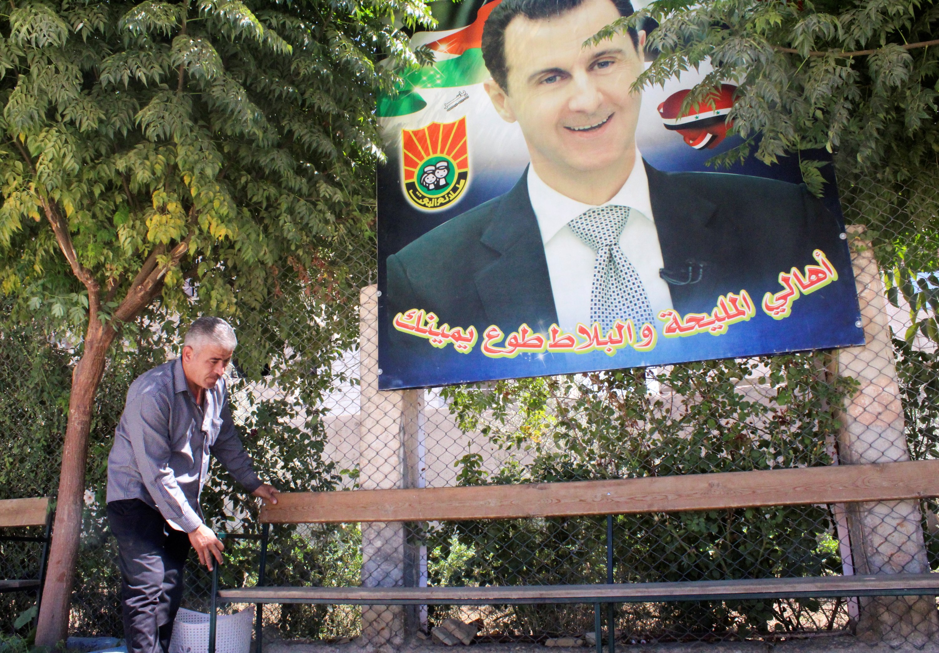 Mohamad Mazhar Doghmosh, a Syrian man who helps in the restoration of Mleiha rural school, adjusts a bench near a poster depicting Syria's President Bashar al-Assad, in Mleiha, Syria, Sept. 14, 2021. (Reuters Photo)