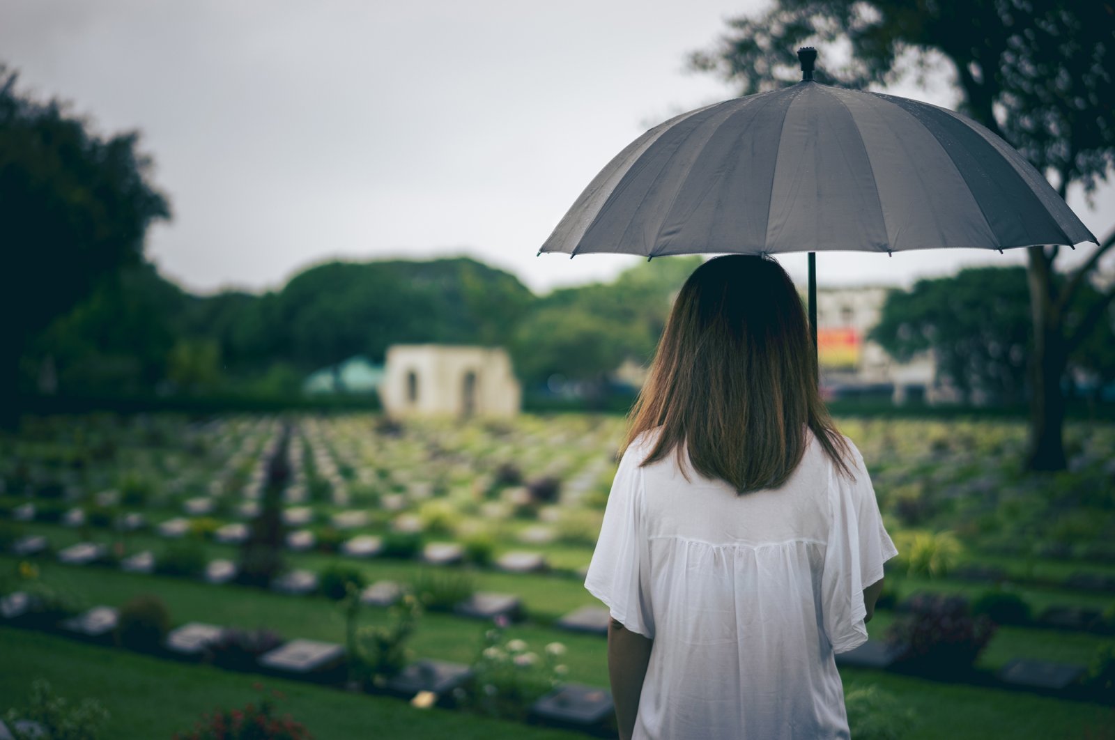 A young woman holds a black umbrella while mourning at a cemetery. (Shutterstock Photo)