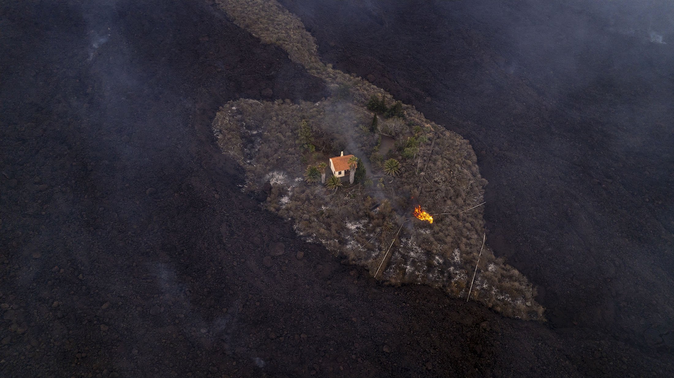 A house remains intact as lava flows after a volcano erupted near Las Manchas on the island of La Palma in the Canaries, Spain, Sept. 20, 2021. (iLoveTheWorld via AP)