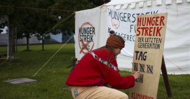 Climate activist Carla Hinrichs makes a line on a wooden board to count the days a small camp of climate activists have been in a hunger strike, near the chancellery in Berlin, Germany, Sept. 22, 2021. (AP Photo)