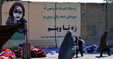 Women walk past a vendor selling secondhand clothes near a defaced mural at a market in Kandahar, Afghanistan, Sept. 22, 2021. (AFP Photo)