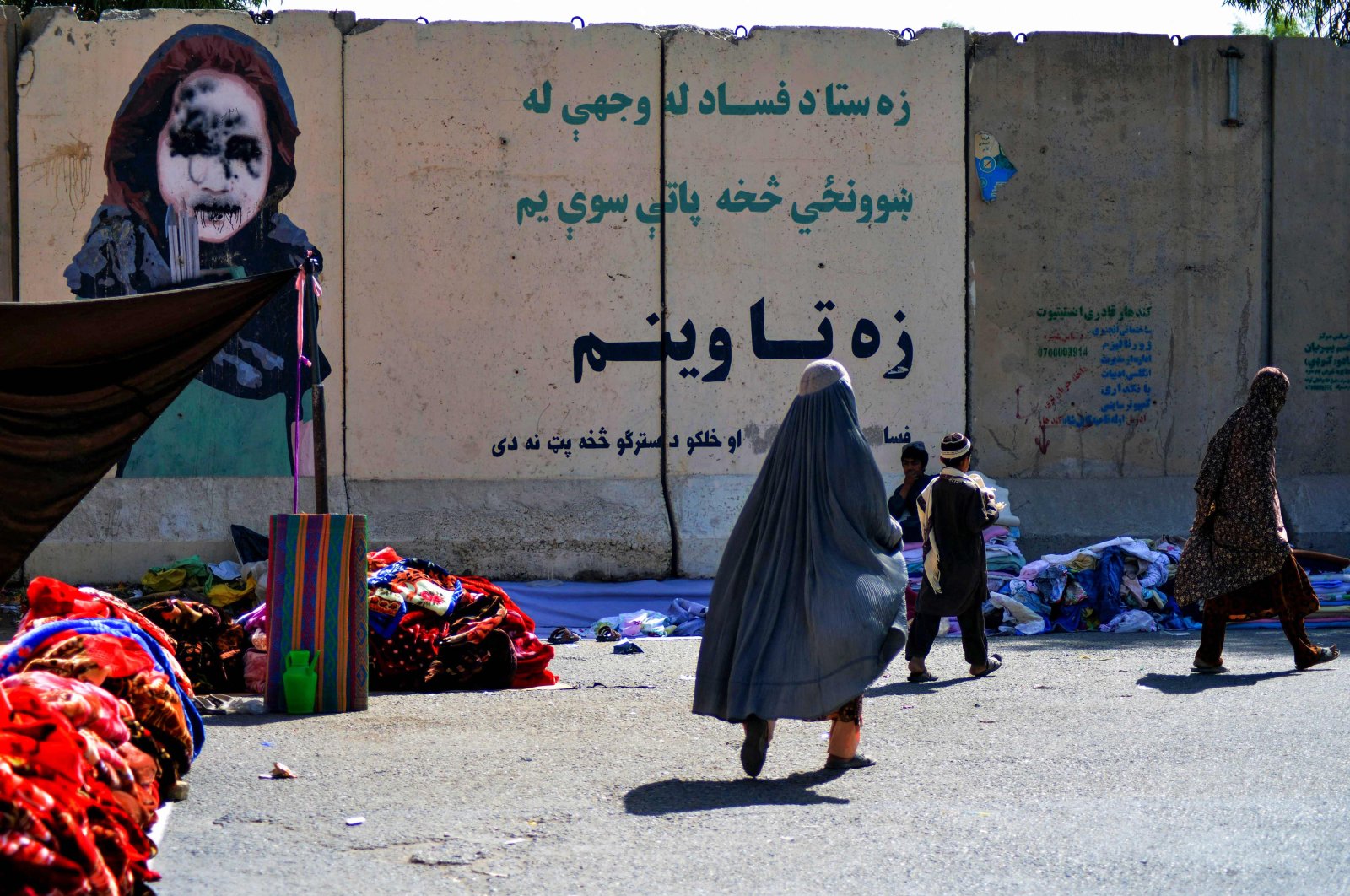 Women walk past a vendor selling secondhand clothes near a defaced mural at a market in Kandahar, Afghanistan, Sept. 22, 2021. (AFP Photo)