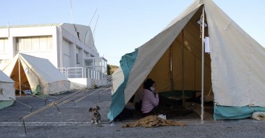 A woman speaks on her cellphone as a dog stands outside a tent in Arkalochori village on the southern island of Crete, Greece, Tuesday, Sept. 28, 2021. (AP Photo)