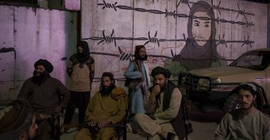 Taliban members sit in front of a mural depicting a woman behind barbed wire in Kabul, Afghanistan, Sept. 21, 2021. (AP Photo)