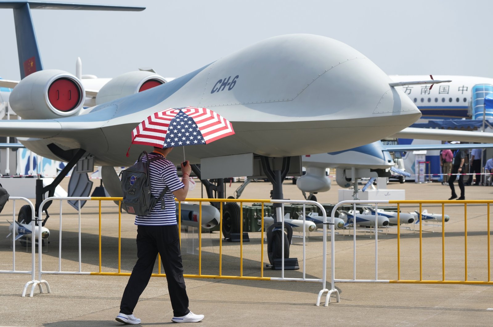 A man carrying an umbrella with the United States flag colors walks past the CH-6 drone during the 13th China International Aviation and Aerospace Exhibition, also known as Airshow China 2021, in Zhuhai in southern China's Guangdong province, Sept. 28, 2021. (AP Photo)