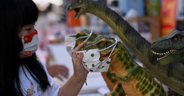 A girl looks at toy dinosaurs with face masks in Qianmen street in Beijing, China, Sept. 21, 2021. (AFP Photo)
