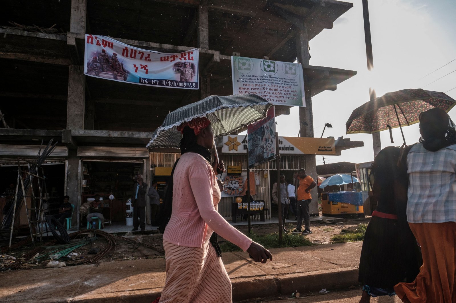 Women with umbrellas walk in front of a sign inviting to vote in a referendum in order to create a new state in southern Ethiopia (R) and a banner inviting to join the army, in the town of Bonga, 100 kilometers southwest of the city of Jimma, Ethiopia, on Aug. 17, 2021. (AFP Photo)