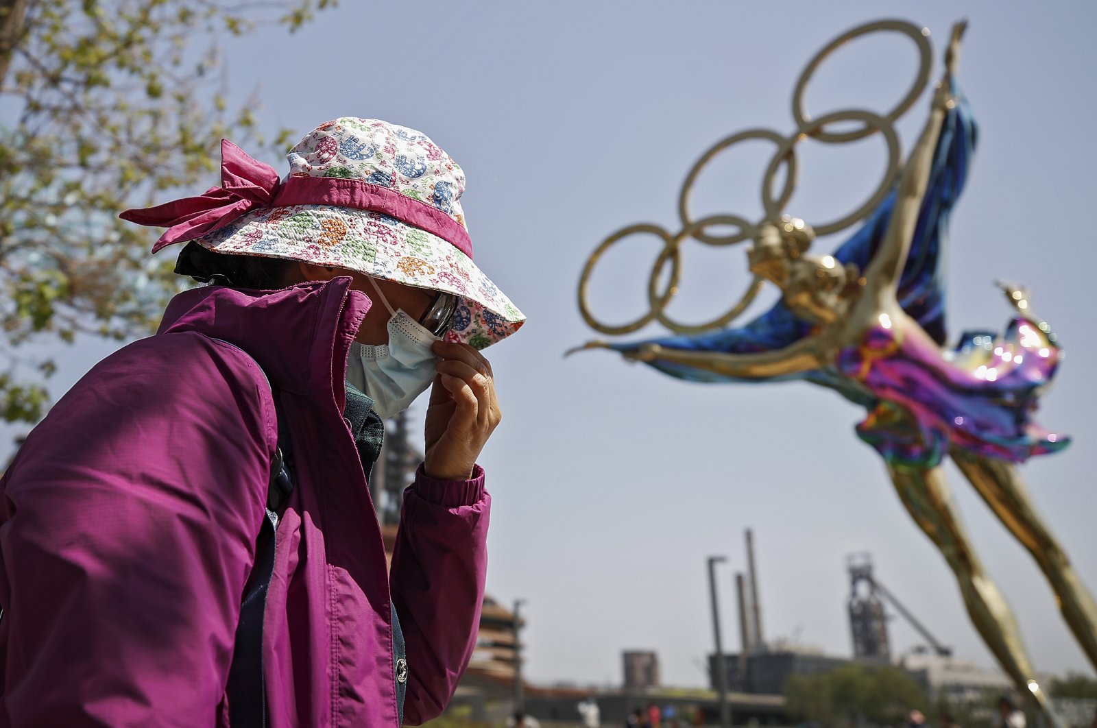 A woman adjusts her face mask as she walks by a statue featuring the Beijing Winter Olympics figure skating at the Shougang Park in Beijing, China, May 2, 2021. (AP Photo)