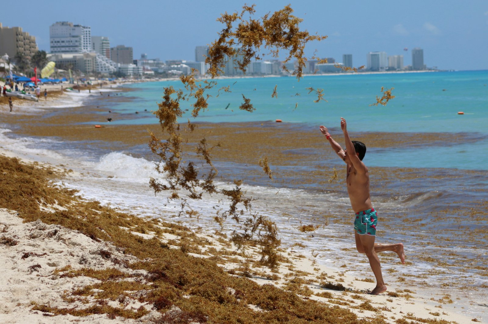 A tourist tosses sargassum into the air at Marlin Beach in Cancun, Mexico, May 30, 2021. (Reuters Photo)