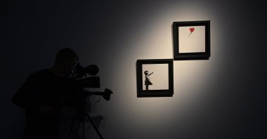 A cameraman stands next to artwork by British artist Banksy titled "Girl and Ballon" (two parts) during a press view at the Christie's auction house in London, Britain, Oct. 1, 2021. (EPA Photo)