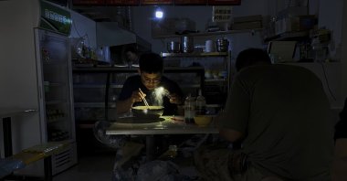 A man uses his smartphone flashlight to light up his bowl of noodles as he eats his breakfast at a restaurant during a blackout in Shenyang in the northeastern Liaoning Province, China, Sept. 29, 2021. (AP Photo)