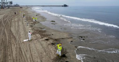 Workers rake up crude oil, after more than 3,000 barrels (126,000 gallons) of crude oil leaked from a ruptured pipeline into the Pacific Ocean in Newport Beach, California, U.S., Oct. 7, 2021. (Reuters Photo)