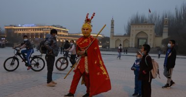 A performer dressed as the monkey god from a Chinese fable walks near a mosque as Uyghur children gaze upon him in Kashgar, Xinjiang Uyghur Autonomous Region, China, March 19, 2021. (AP Photo)