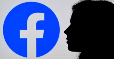 In this photo illustration, a person looks at a smartphone with a Facebook App logo displayed on the background, in Arlington, Virginia, U.S., Aug. 17, 2021. (AFP Photo)