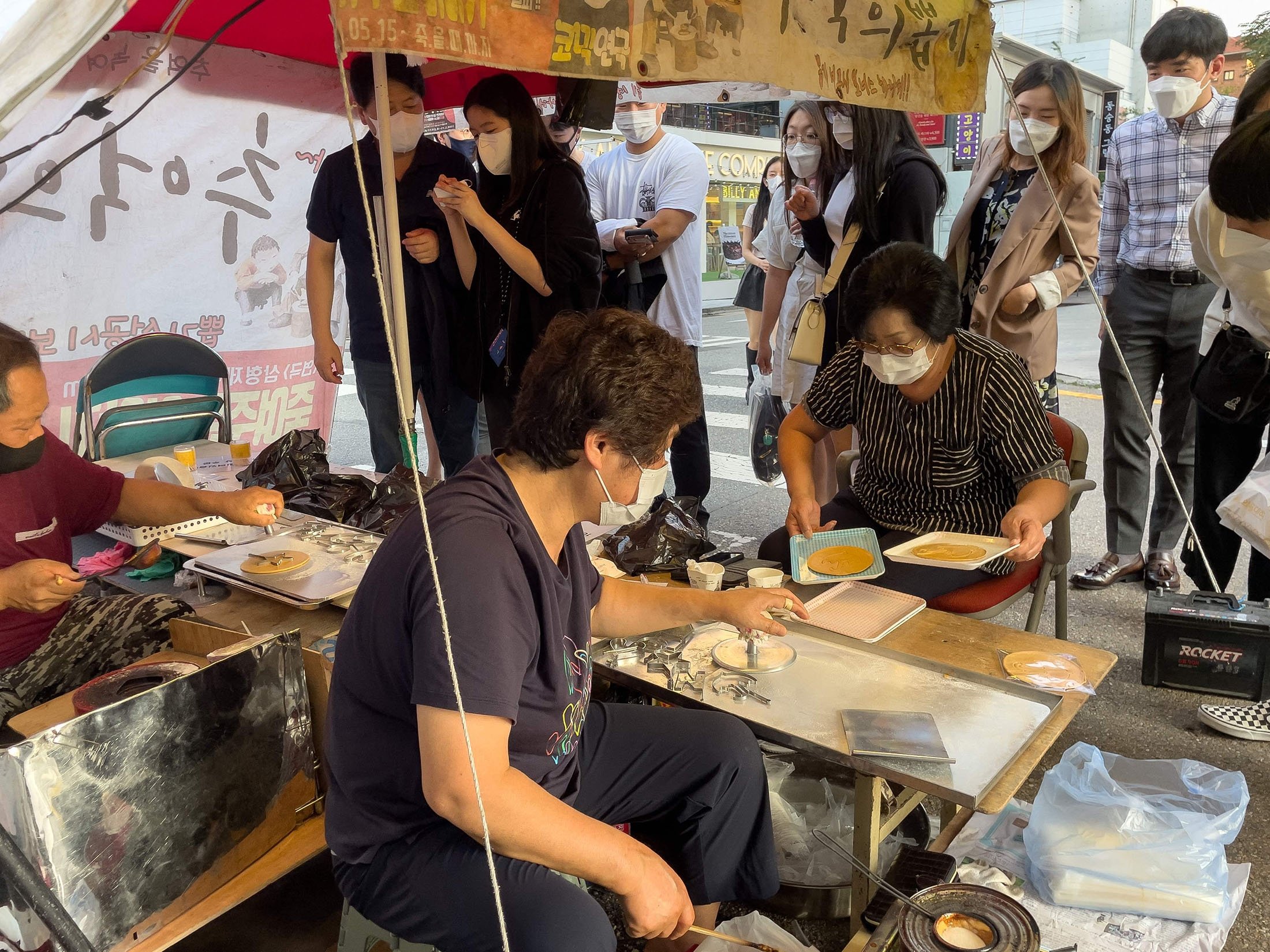 Customers wait in line as street vendor Jung Jung-soon (C) and her husband Lim Chang-joo (L) sell freshly made dalgonas, a crisp sugar candy featured in the Netflix smash hit series "Squid Game," in Seoul, South Korea, Oct. 10, 2021. (AFP Photo)
