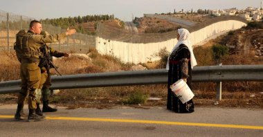 A Palestinian woman stands with others (not pictured) as they gather near an Israeli army checkpoint and wait to reach their olive fields on the other side of Israel's separation barrier (background), near the village of Bait A'wa on the outskirts of the West Bank city of Hebron, occupied Palestine, Oct. 13, 2021. (AFP Photo)