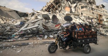 A Palestinian man transports children in a tricycle past the Al-Shuruq building, destroyed by an Israeli airstrike, in Gaza City, the Gaza Strip, Palestine, May 21, 2021. (AFP Photo)