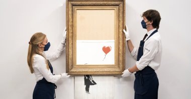 Art handlers at Sotheby's auction house hold Banksy's "Love is in the Bin," before it returns to auction at Sotheby's, London, U.K., Sept. 3, 2021. (AP Photo)