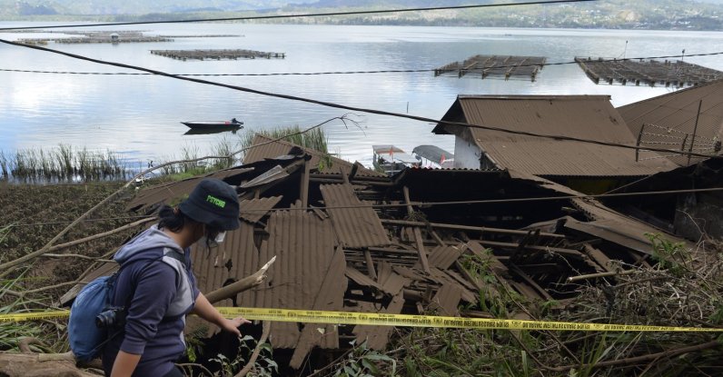 A woman walks past houses by Lake Batur that were damaged by an earthquake-triggered landslide in Bangli, on the island of Bali, Indonesia, Oct. 16, 2021. (AP Photo)