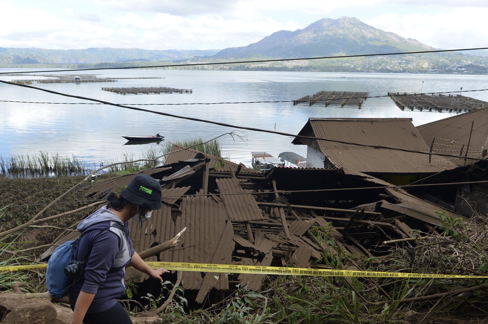 A woman walks past houses by Lake Batur that were damaged by an earthquake-triggered landslide in Bangli, on the island of Bali, Indonesia, Oct. 16, 2021. (AP Photo)