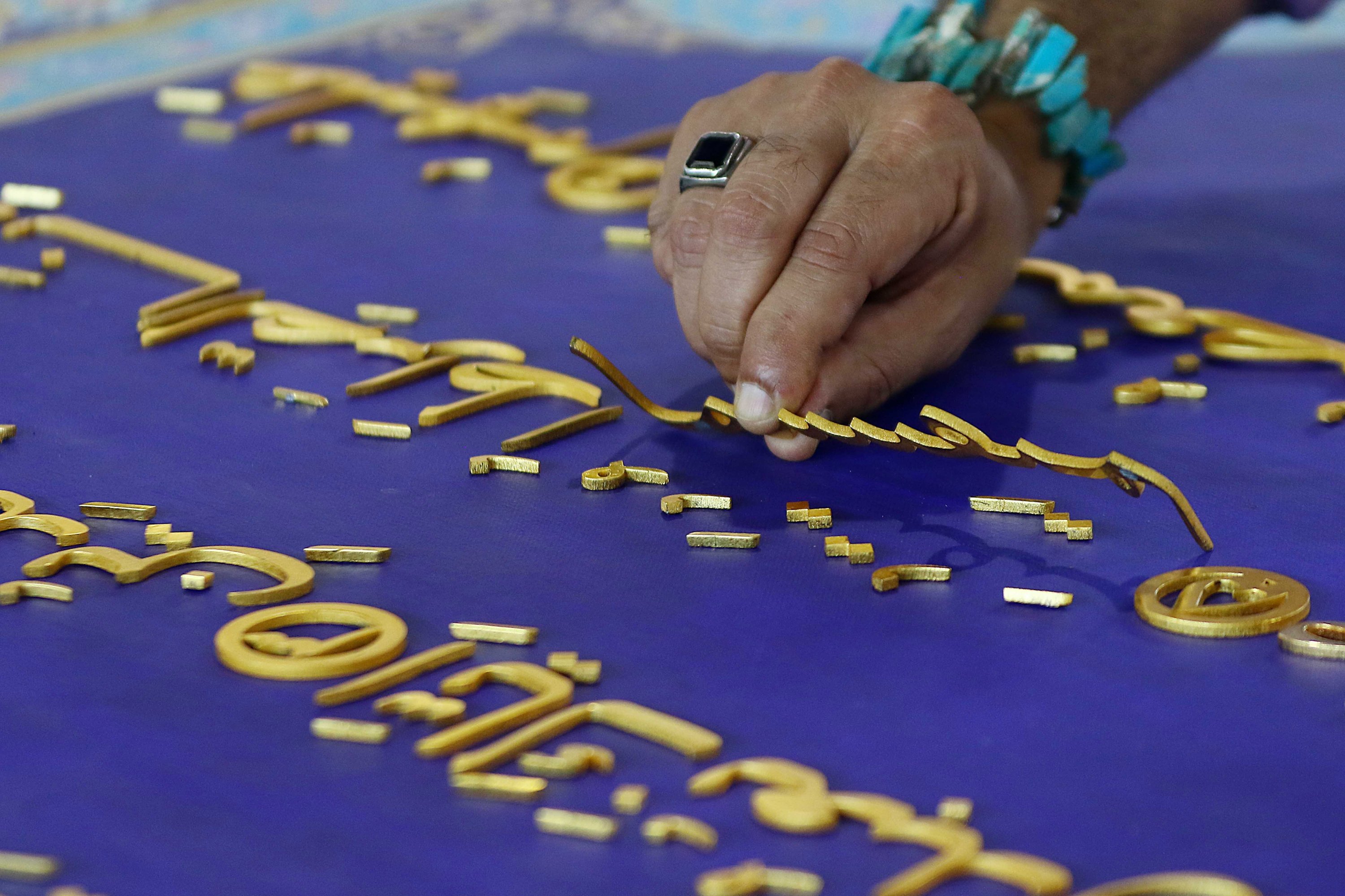 Pakistani artist Shahid Rassam works on the calligraphy of Quran verses on canvas with aluminum and gold-plated words. (EPA Photo) 