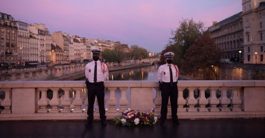Police officers stand near a wreath of flowers on the Saint Michel bridge during a ceremony to commemorate France's brutal repression of an Oct. 17, 1961, anticolonialism demonstration where at least 120 Algerians were killed, Paris, France, Oct. 17, 2021. (AFP Photo)