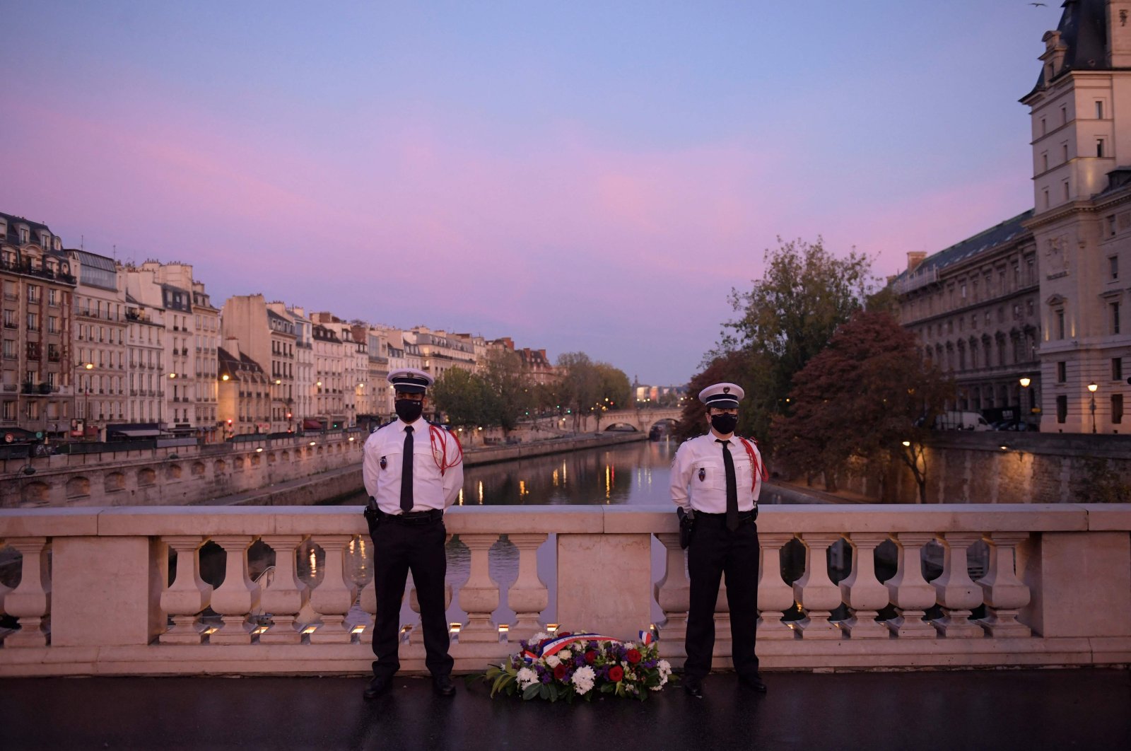 Police officers stand near a wreath of flowers on the Saint Michel bridge during a ceremony to commemorate France's brutal repression of an Oct. 17, 1961, anticolonialism demonstration where at least 120 Algerians were killed, Paris, France, Oct. 17, 2021. (AFP Photo)