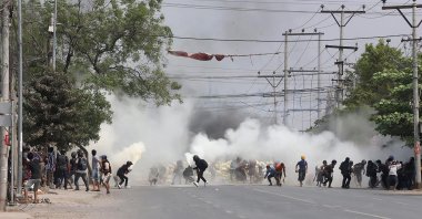 Protesters run from tear gas fired by security forces, as some demonstrators also let off fire extinguishers, next to a barricade set up during the demonstration against the military coup in Mandalay, Myanmar, March 15, 2021. (AFP Photo )