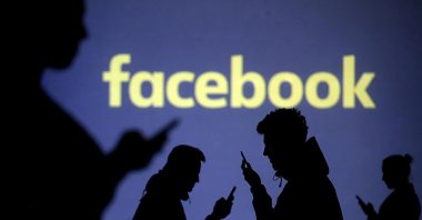 Silhouettes of people looking at their phones against the Facebook logo, Nov. 24, 2018. (Sabah Archive Photo)