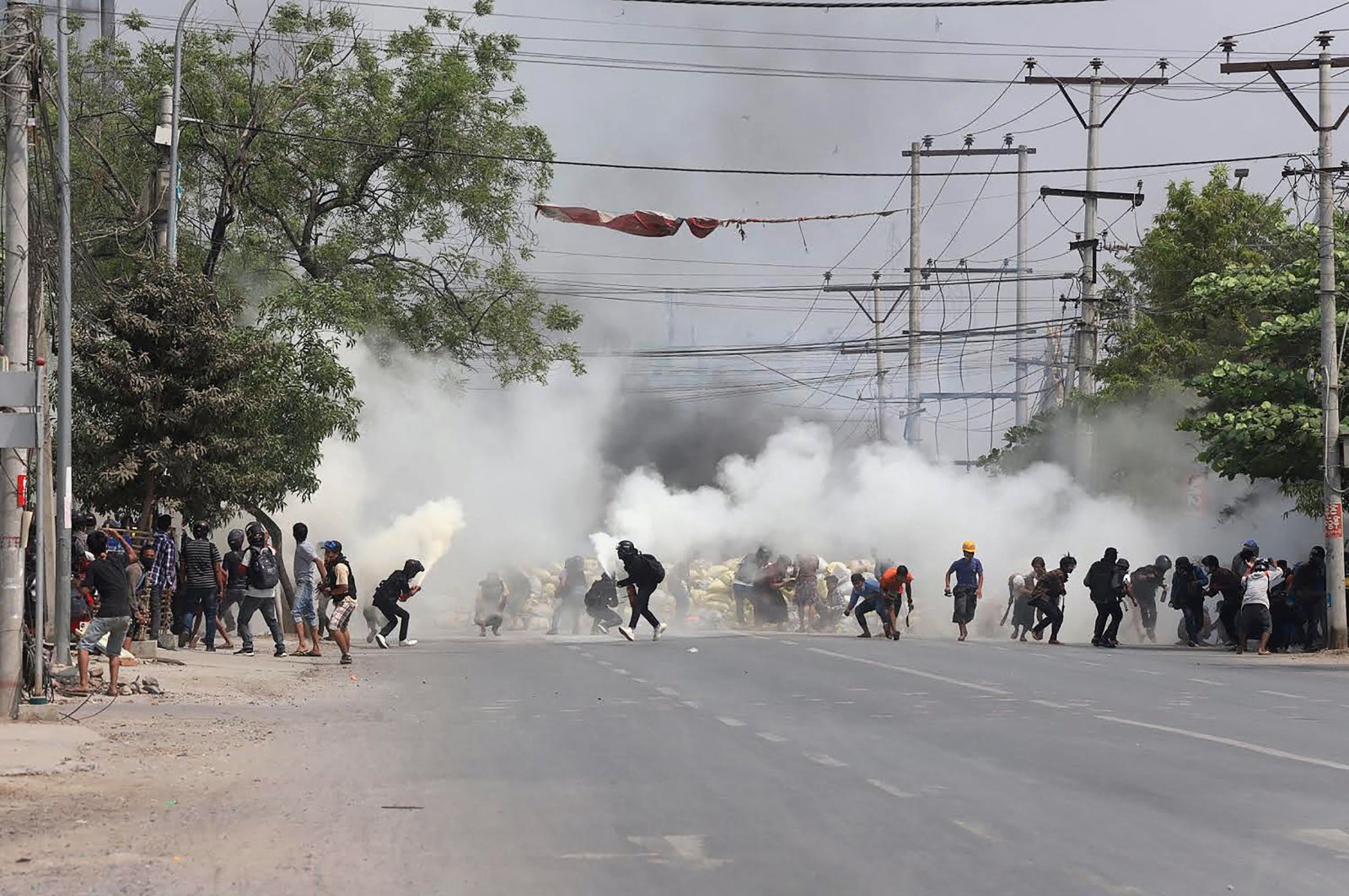 Protesters run from tear gas fired by security forces, as some demonstrators also let off fire extinguishers, next to a barricade set up during the demonstration against the military coup in Mandalay, Myanmar, March 15, 2021. (AFP Photo )