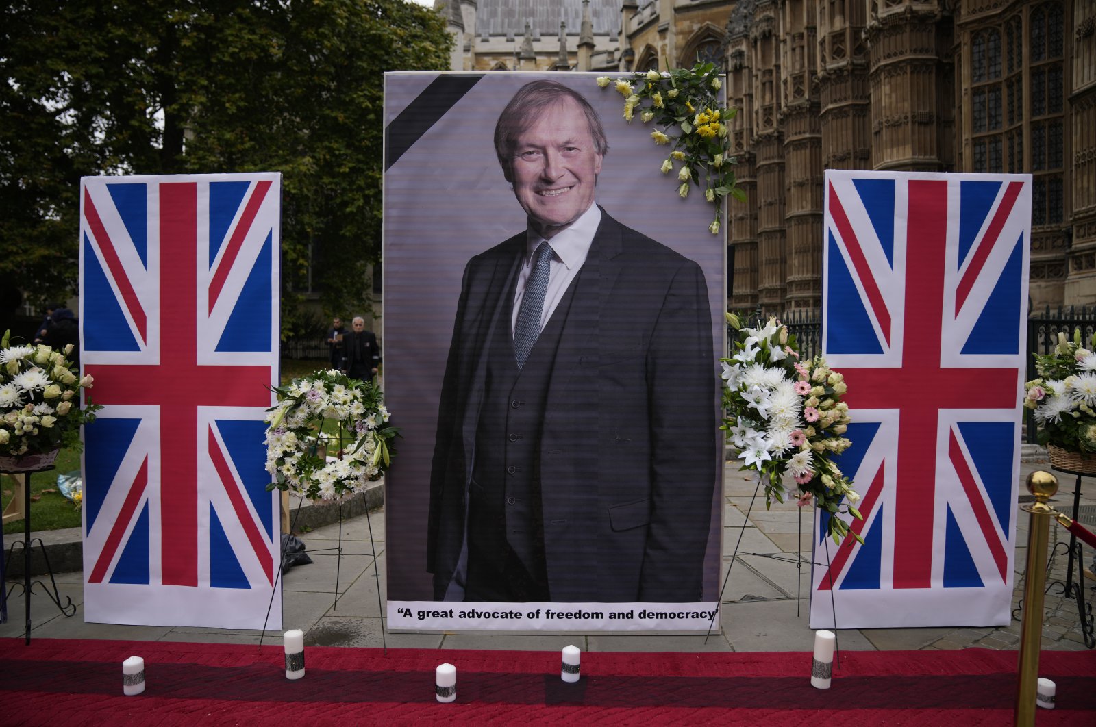 An image of British Member of Parliament David Amess is displayed opposite the Houses of Parliament in London, placed there as a memorial by supporters of the National Council of Resistance of Iran (NCRI), London, U.K., Oct. 18, 2021. (AP Photo)