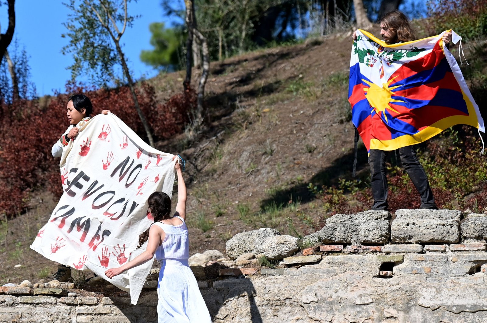 Three protesters unfurl a banner and a Tibetan flag during the flame-lighting ceremony for the Beijing 2022 Winter Olympics at the Ancient Olympia archeological site, birthplace of the ancient Olympics in southern Greece, Oct. 18, 2021. (AFP Photo)
