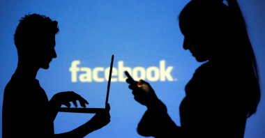 People are silhouetted as they pose with laptops in front of a screen projected with a Facebook logo, in this picture illustration taken in Zenica, Bosnia-Herzegovina, Oct. 29, 2014. (Reuters Photo)