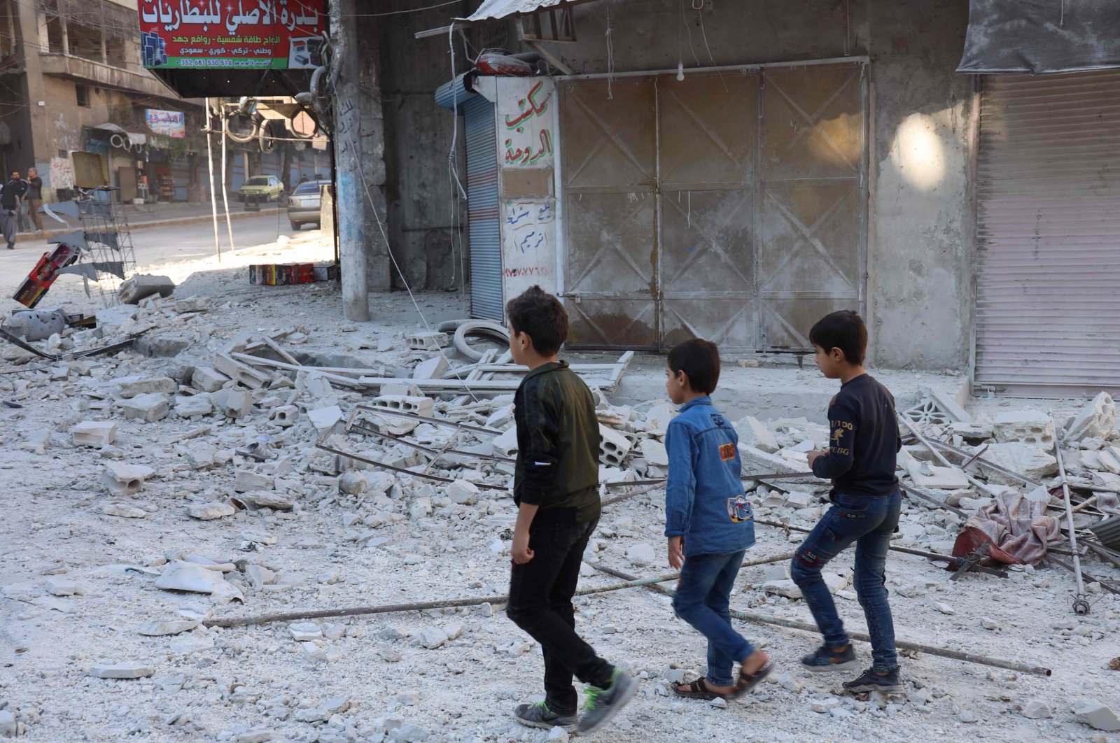 People walk past debris at the site of shelling in the Syrian town of Ariha in the opposition-held northwestern Syrian Idlib province on October 20, 2021. (AFP Photo)
