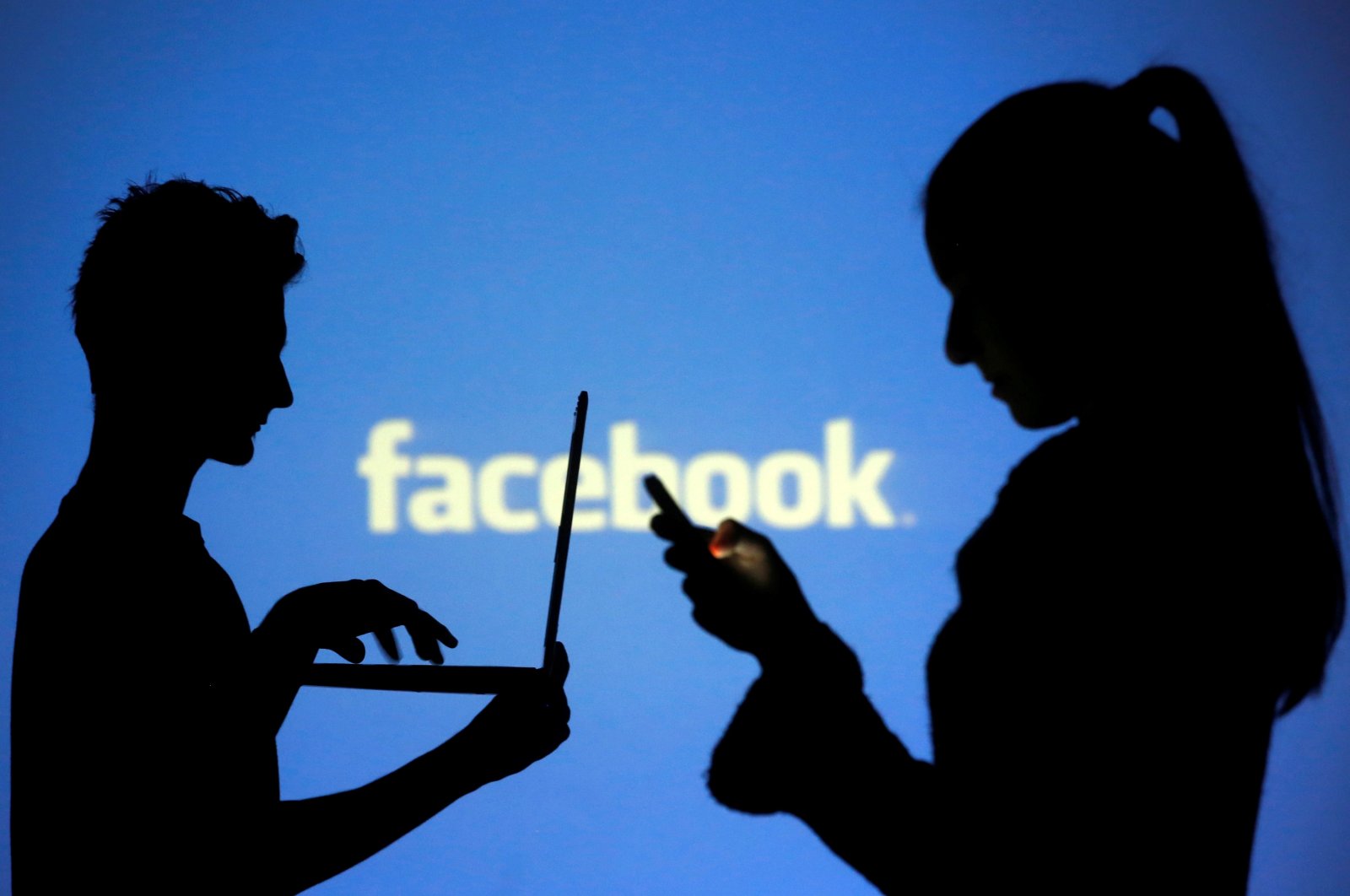 People are silhouetted as they pose with laptops in front of a screen projected with a Facebook logo, in this picture illustration taken in Zenica, Bosnia-Herzegovina, Oct. 29, 2014. (Reuters Photo)