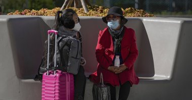 Women wearing face masks to help curb the spread of the coronavirus chat to each other on a bench outside a shopping mall in Beijing, China, Oct. 21, 2021. (AP Photo)