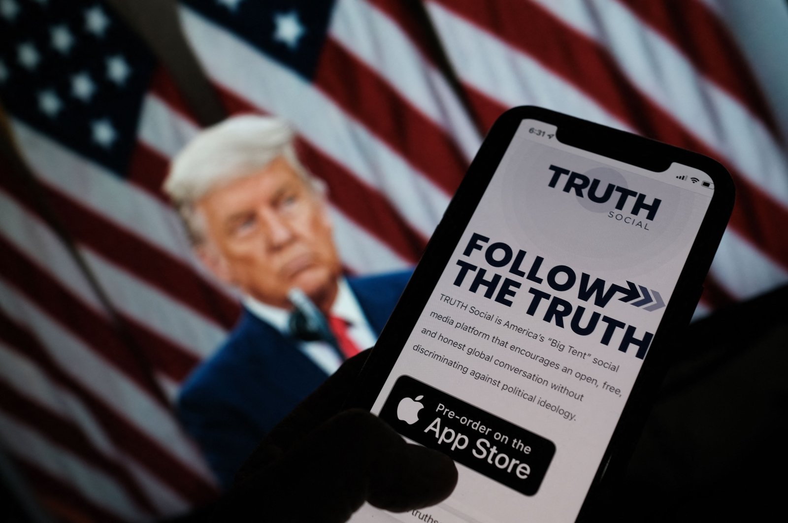 This illustration photo shows a person checking the app store on a smartphone for "Truth Social," with a photo of former U.S. President Donald Trump on a computer screen in the background, in Los Angeles, U.S., Oct. 20, 2021. (AFP Photo)