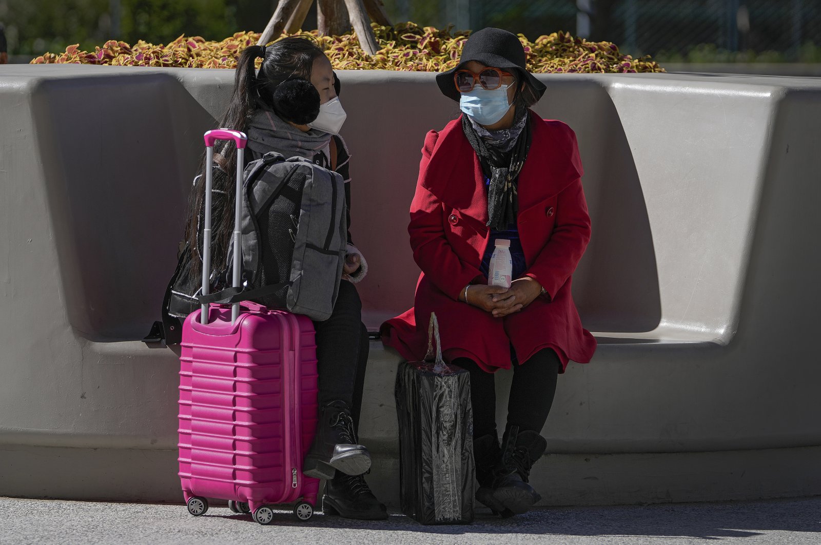 Women wearing face masks to help curb the spread of the coronavirus chat to each other on a bench outside a shopping mall in Beijing, China, Oct. 21, 2021. (AP Photo)