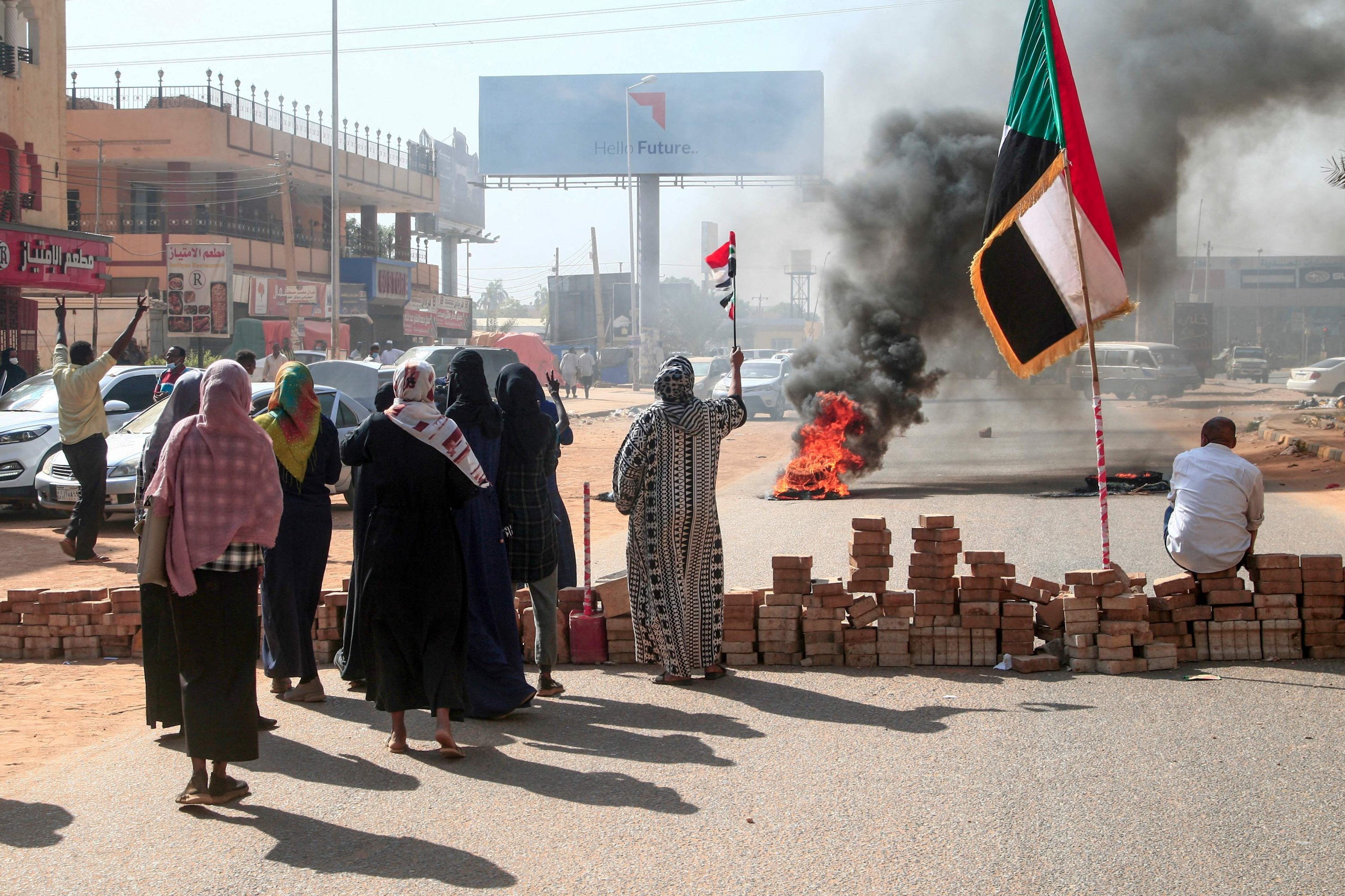 Sudanese protesters lift national flags next to a brick roadblock during a demonstration in the capital Khartoum, on Oct. 25, 2021, to denounce overnight detentions by the army of members of Sudan