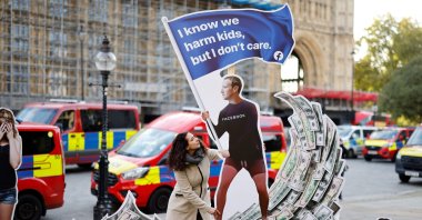 A demonstrator poses with an installation depicting Facebook founder Mark Zuckerberg surfing on a wave of cash and surrounded by distressed teenagers, during a protest opposite the Houses of Parliament in central London, U.K., Oct. 25, 2021. (AFP Photo)