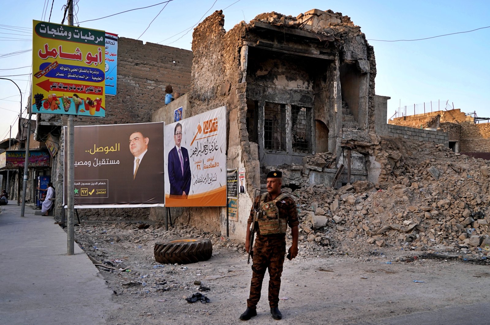 An Iraqi federal policeman stands guard near campaign posters for parliamentary elections are displayed near destroyed buildings from fighting between Iraqi forces and the Daesh terror group in Mosul, Iraq, Oct. 3, 2021. (AP Photo)