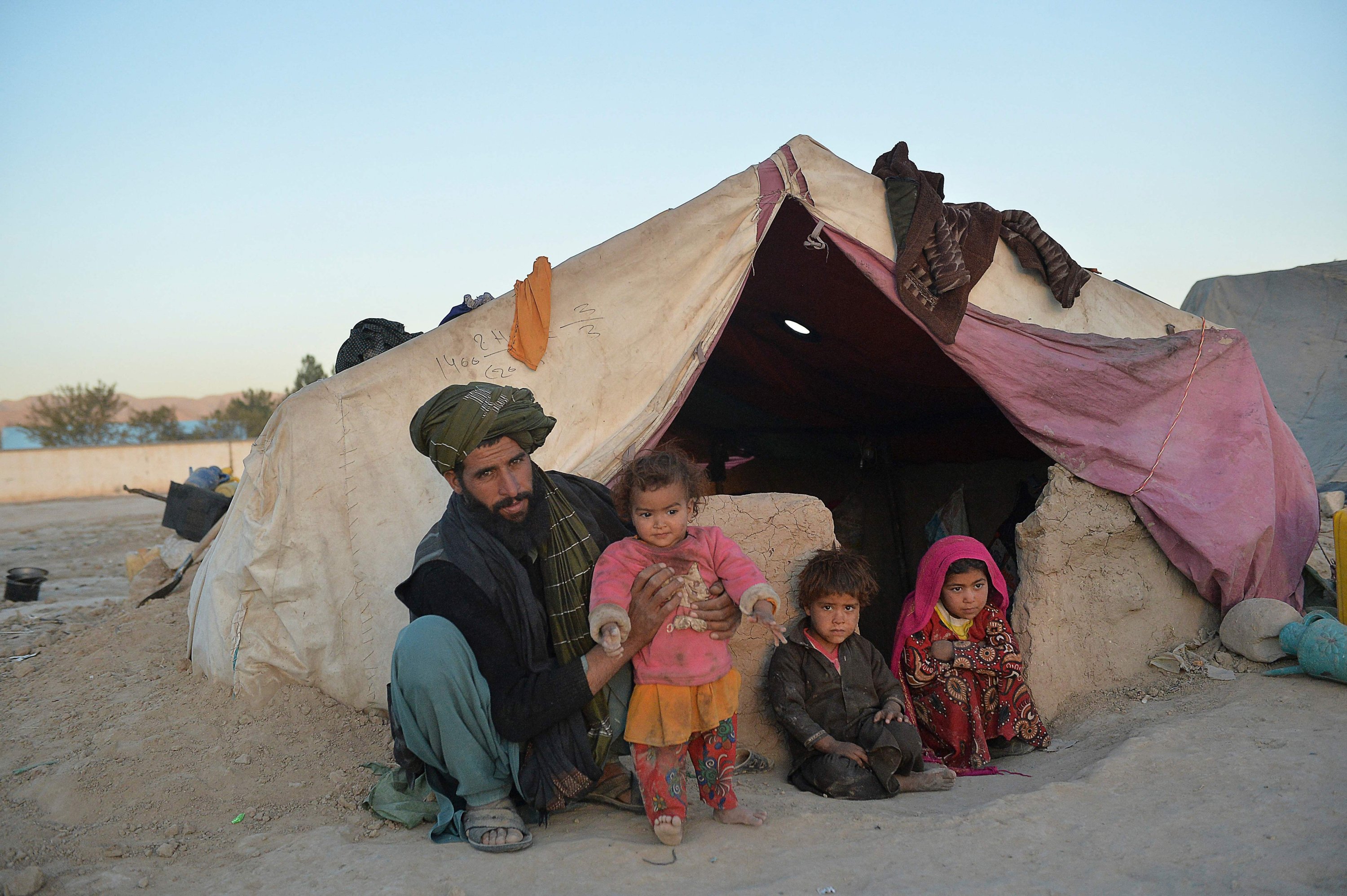 Children Farishteh (R) and Shokriya (2L), who were recently sold to the families of their future husbands, sitting with their father outside a tent at the Shamal Darya Internally Displaced People (IDP) camp in Qala-i-Naw, Badghis Province, Afghanistan, Oct. 14, 2021. (AFP Photo)