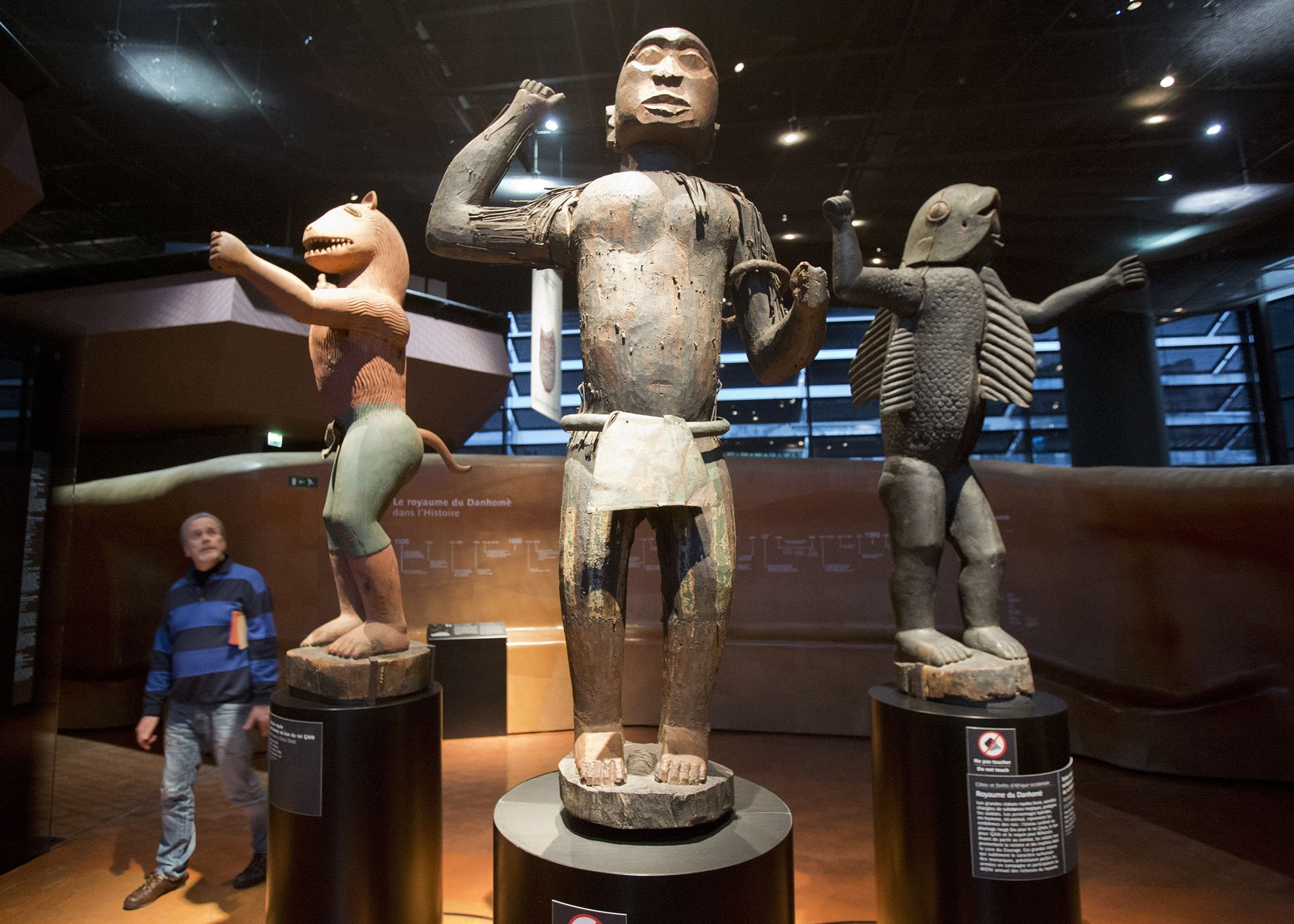 A visitor looks at wooden royal statues of the Dahomey kingdom, dated 19th century, at the Quai Branly – Jacques Chirac museum, in Paris, France, Nov. 23, 2018. (AP Photo)