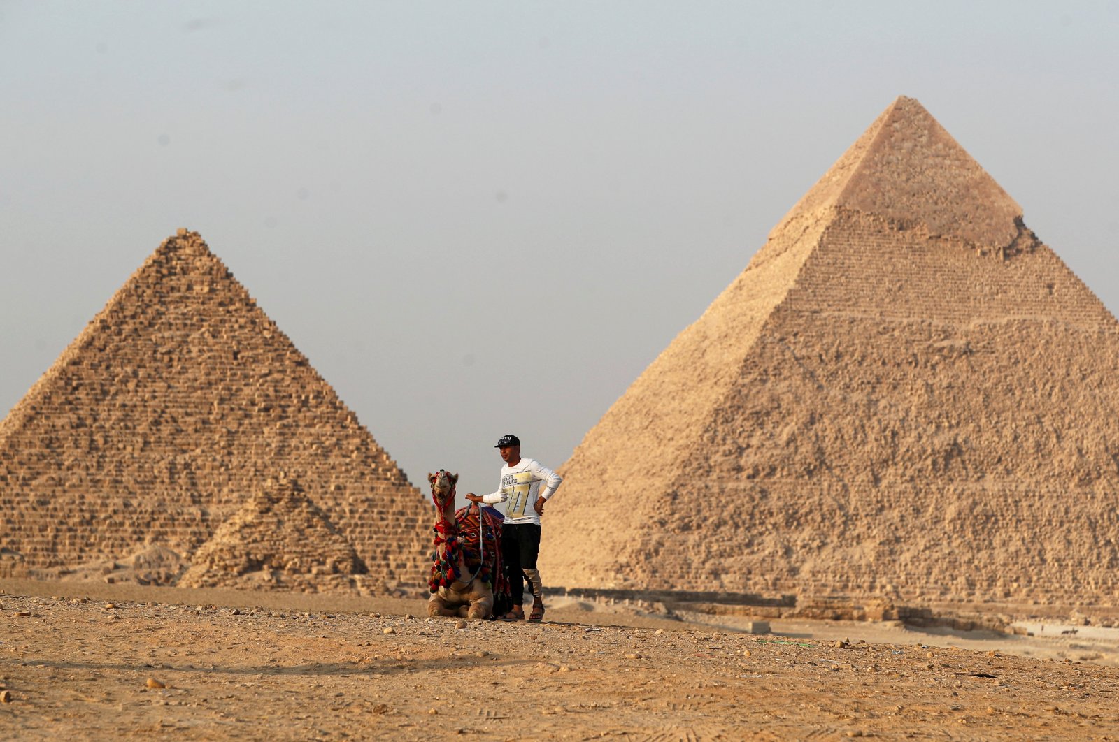 A man with his camel waits for tourists in front of the famed pyramids of Giza, on the outskirt of Cairo, Egypt, Oct. 23, 2021. (Reuters Photo)