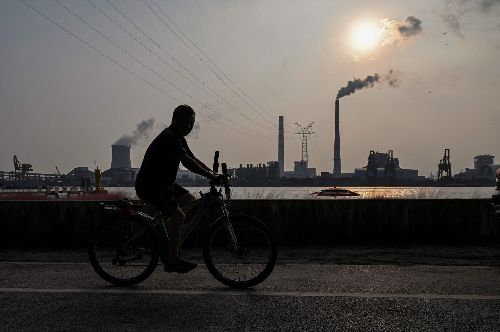 A man rides a bicycle on a promenade along the Huangpu river across from the Wujing Coal-Electricity Power Station in Shanghai, China, Sept. 28, 2021. (AFP Photo)