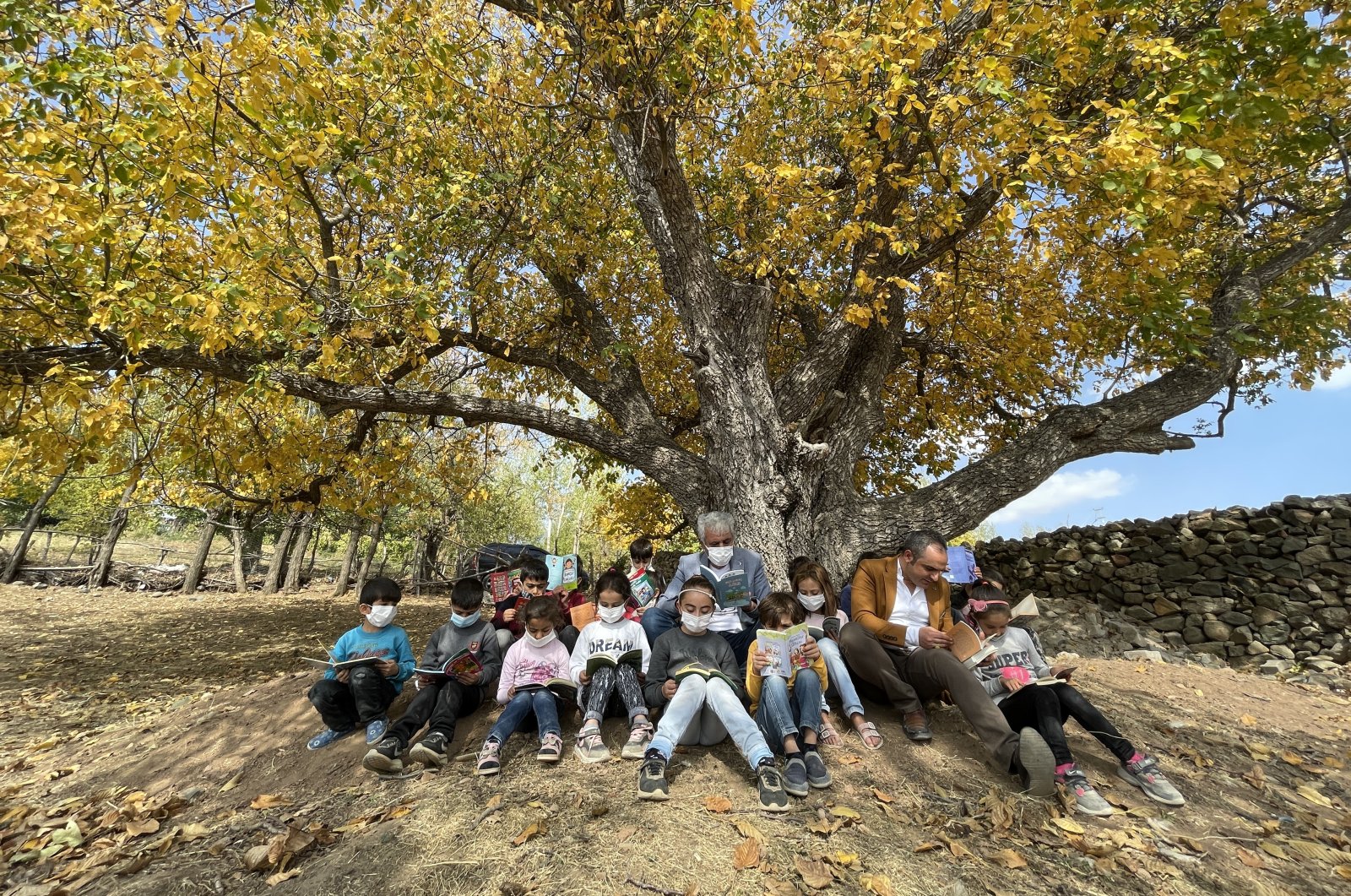 Cuma Karaaslan (C) reads books with children under a tree in the village of Çavuşlar, in Bingöl, eastern Turkey, Oct. 26, 2021. (AA PHOTO)
